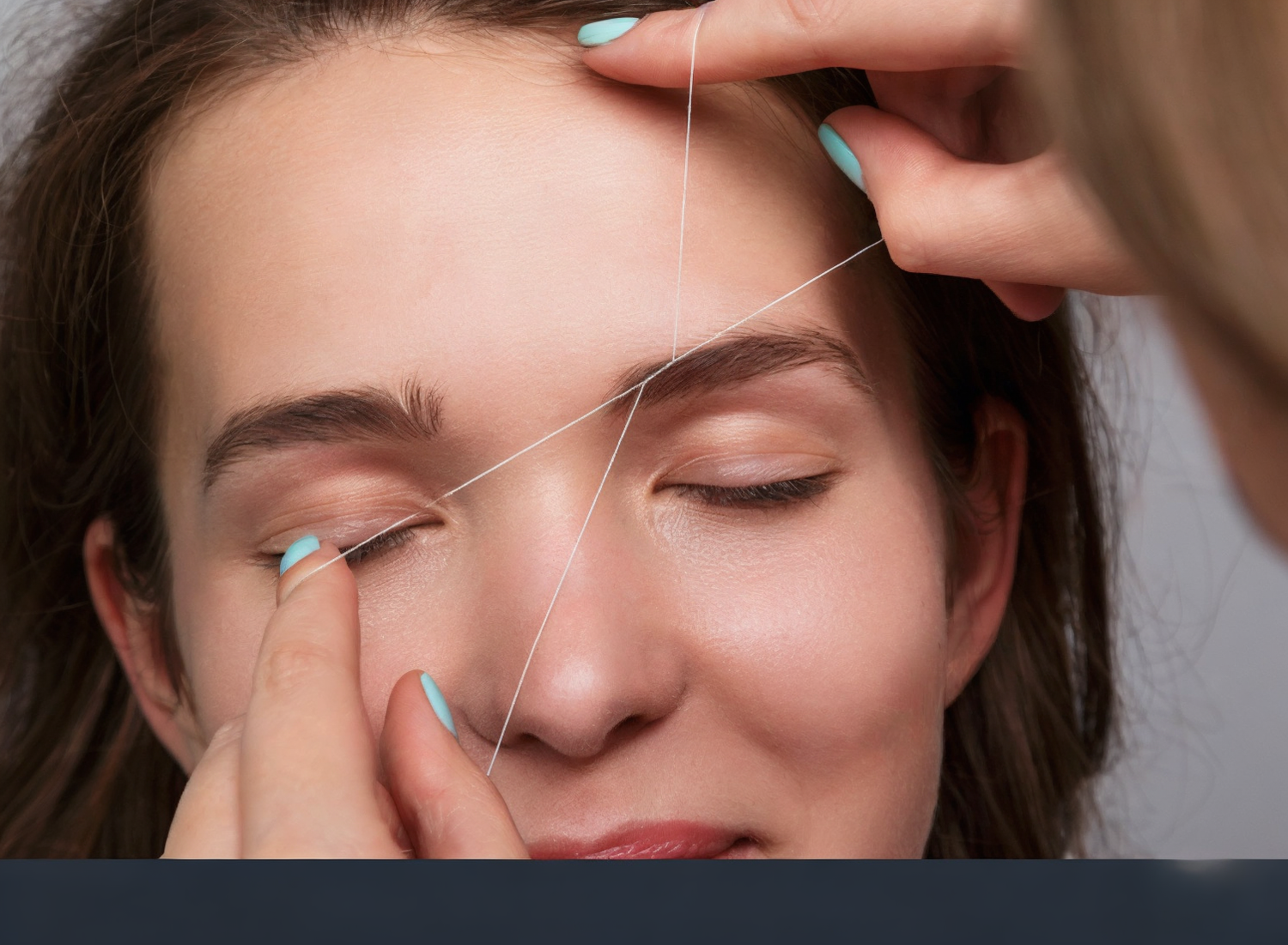 "Close-up of a woman receiving eyebrow threading with eyes closed, showing the thread technique used by a beautician for precise hair removal at a salon."